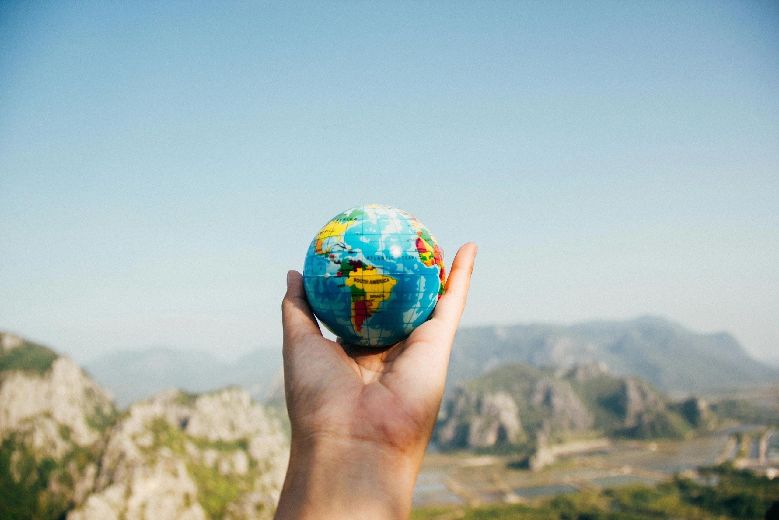 Hand holding a colorful globe against a mountain landscape